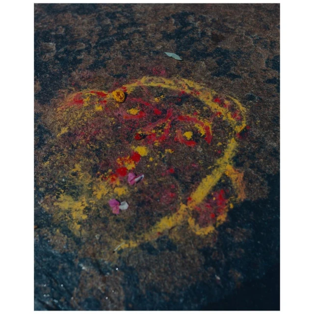 Red and yellow powder design on a dark stone surface featuring a circular outline and floral accents, photographed with a high angle.