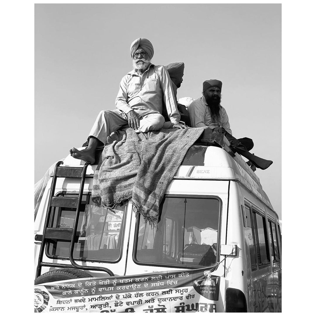 Black and white shot shows group of men sitting on top of a white van under a clear sky. Farmers' protest. 
