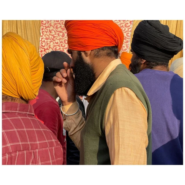 Three Sikh men in turbans and traditional clothing, possibly at an outdoor gathering or event, with a blurry background.
