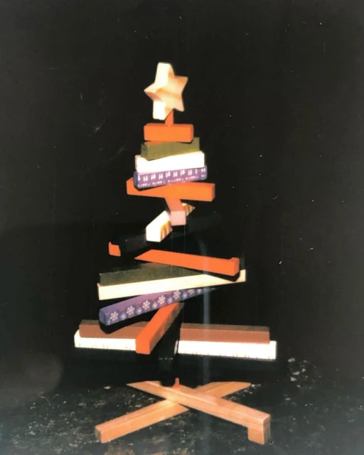 Handmade Christmas tree decoration with wooden blocks of orange, green, white and brown stacked on top of each other with a star on top.