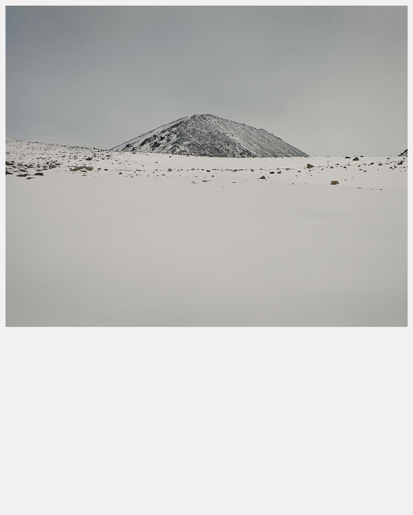 Snow-covered mountain landscape featuring a single, prominent peak under a cloudy sky, highlighting winter's stark beauty and serene isolation.