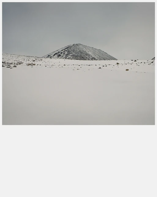 Snow-covered mountain landscape featuring a single, prominent peak under a cloudy sky, highlighting winter's stark beauty and serene isolation.