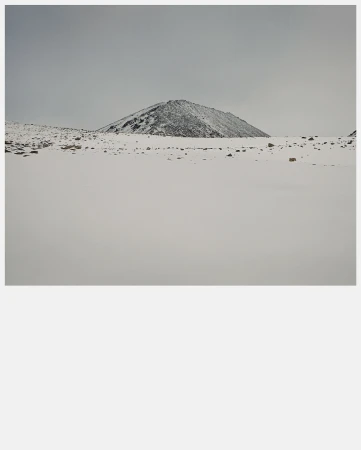 Snow-covered mountain landscape featuring a single, prominent peak under a cloudy sky, highlighting winter's stark beauty and serene isolation.