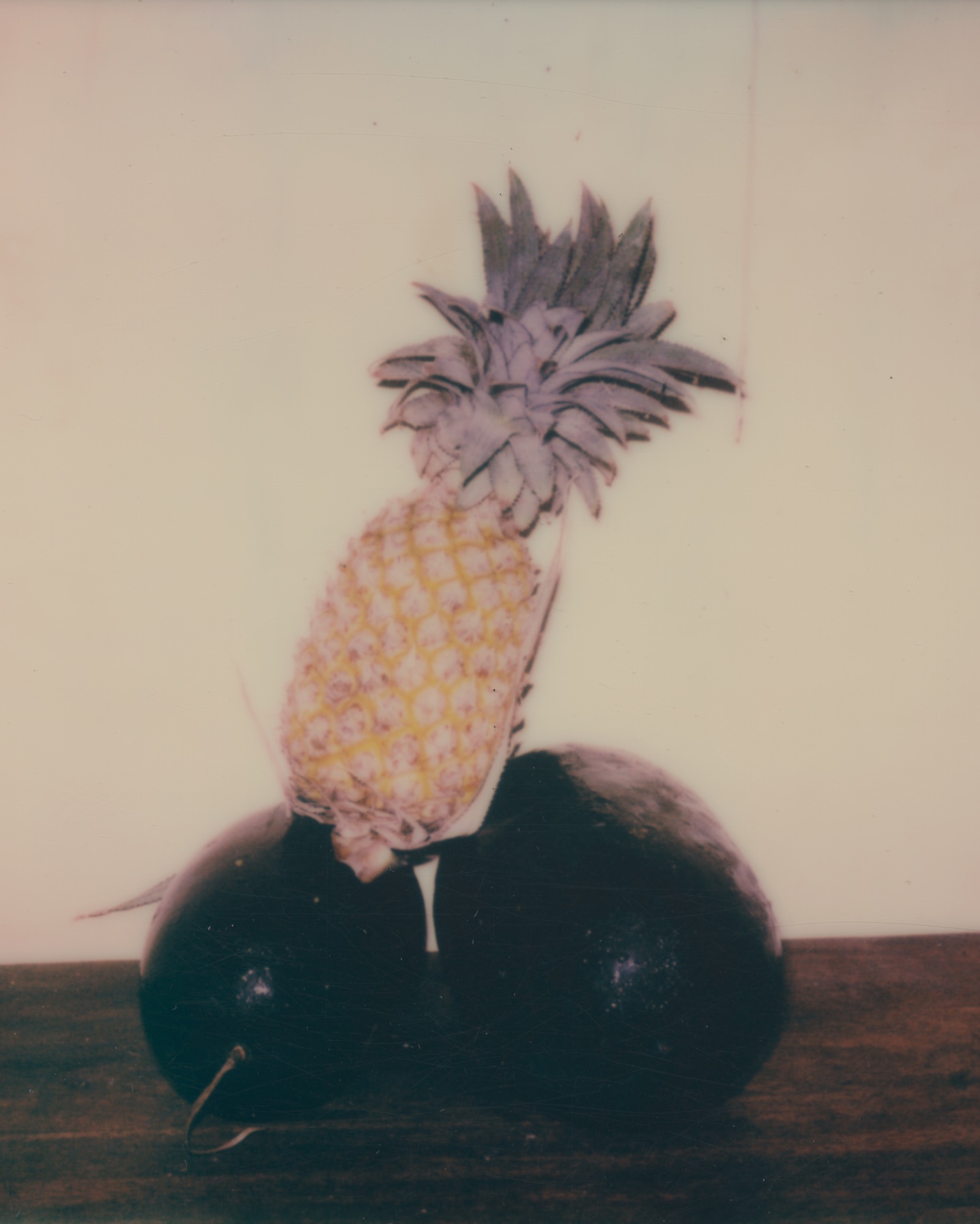Still life shot of pineapple and avocado pair on a wooden table. Close-up of fruits with textured skin and foliage on top of the pineapple.
