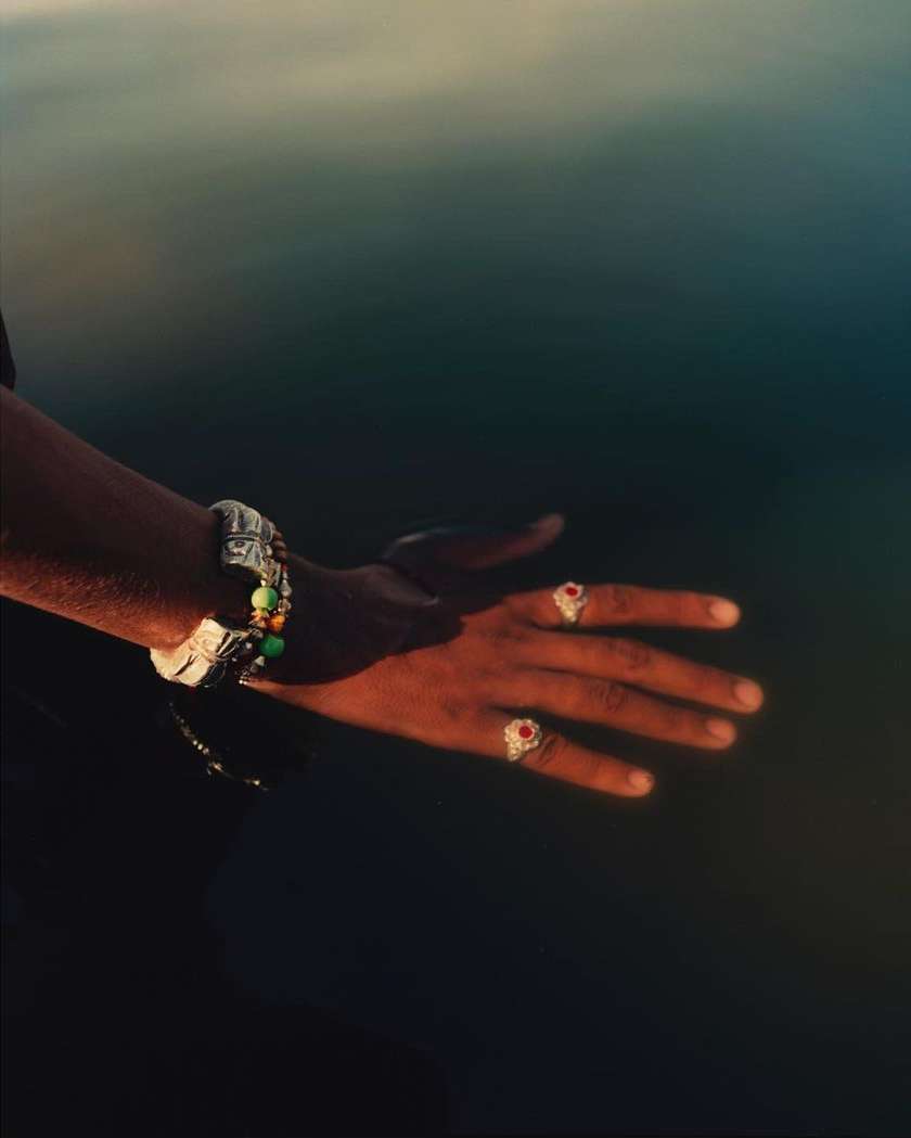 Close-up of a person's hands adorned with rings and bracelets, illuminated by golden sunlight against a blurred, dark background.