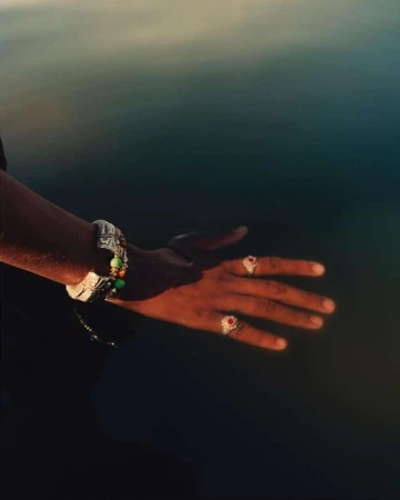 Close-up of a person's hands adorned with rings and bracelets, illuminated by golden sunlight against a blurred, dark background.