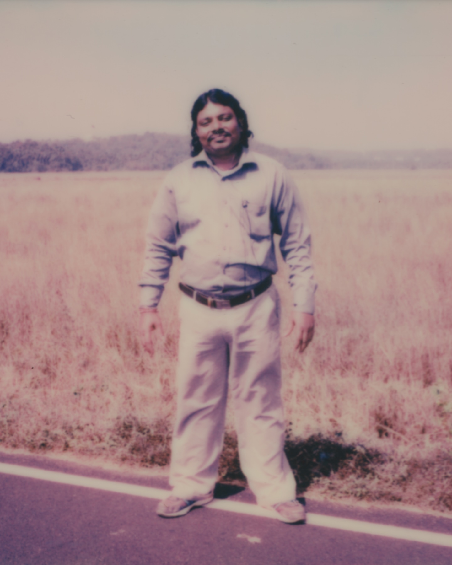 Outdoor portrait of a man in casual clothes on a road with a field and trees in the background, captured in a vintage style.