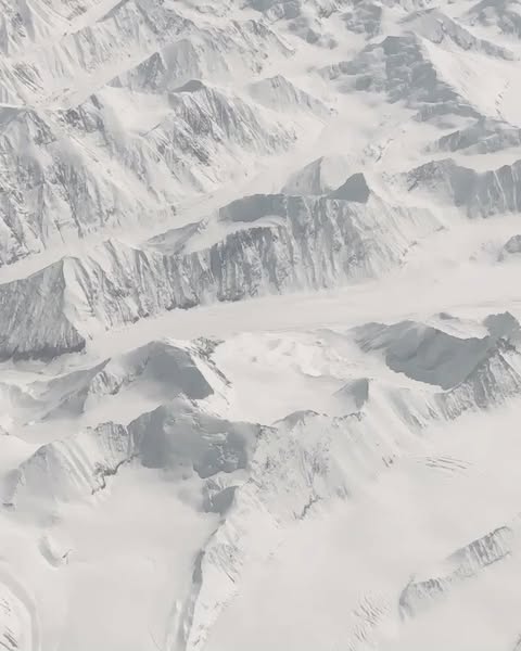Aerial view of snow-covered mountain range, displaying the textures, shapes, and patterns of the winter landscape.