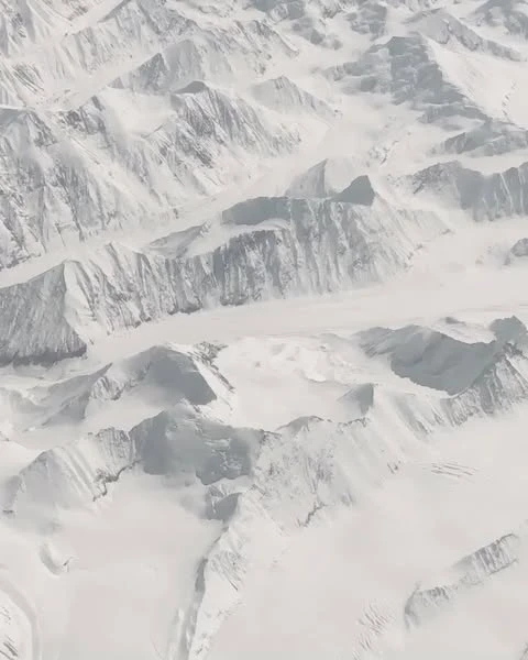 Aerial view of snow-covered mountain range, displaying the textures, shapes, and patterns of the winter landscape.