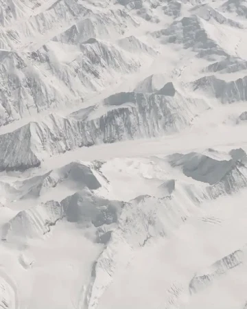 Aerial view of snow-covered mountain range, displaying the textures, shapes, and patterns of the winter landscape.