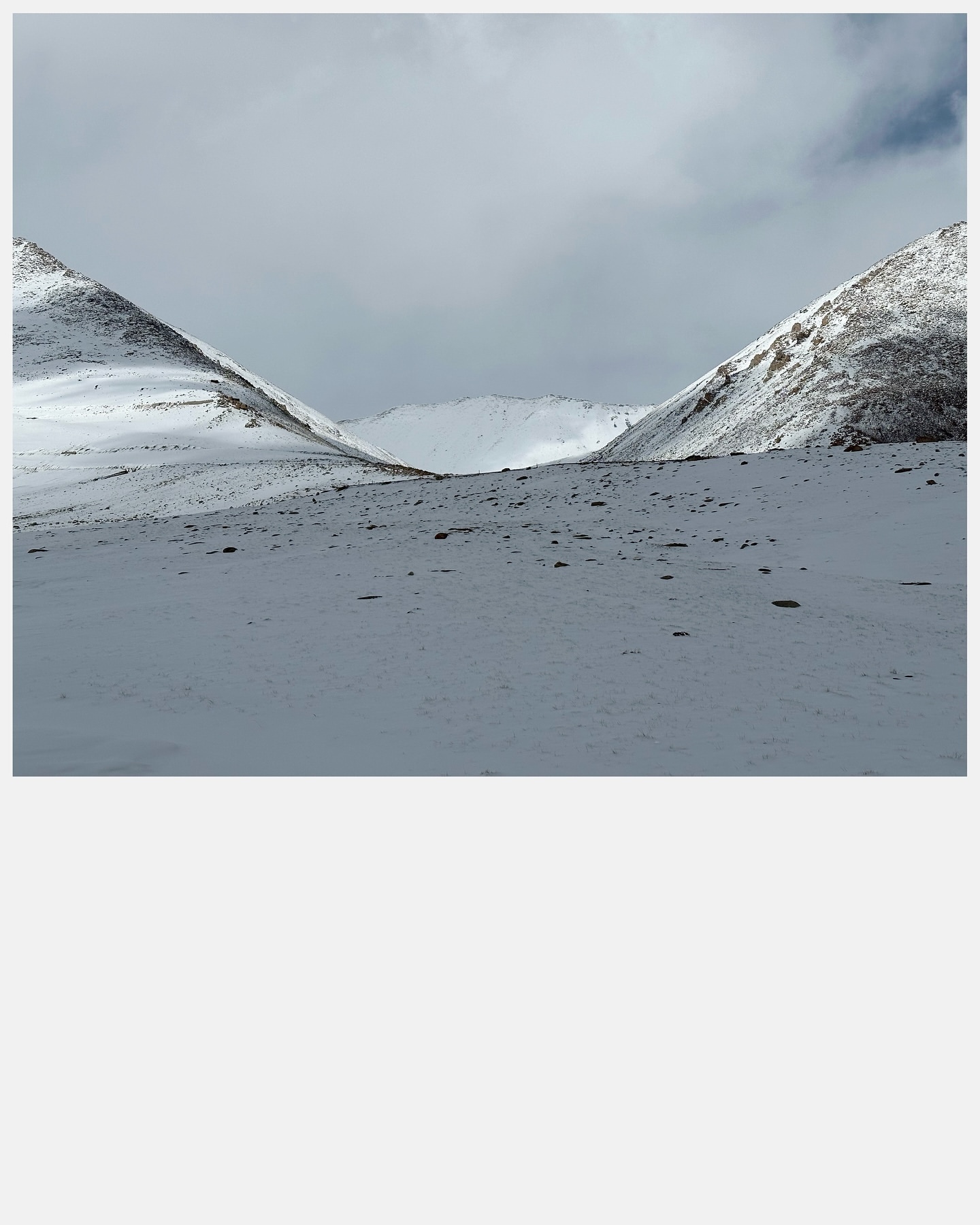 Snowy mountain range under an overcast sky. The landscape features peaks and valleys blanketed in fresh snow, creating a monochromatic scene.