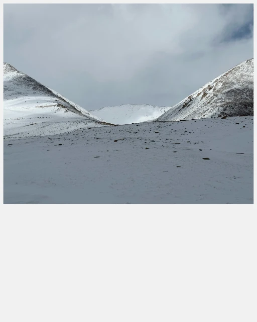 Snowy mountain range under an overcast sky. The landscape features peaks and valleys blanketed in fresh snow, creating a monochromatic scene.
