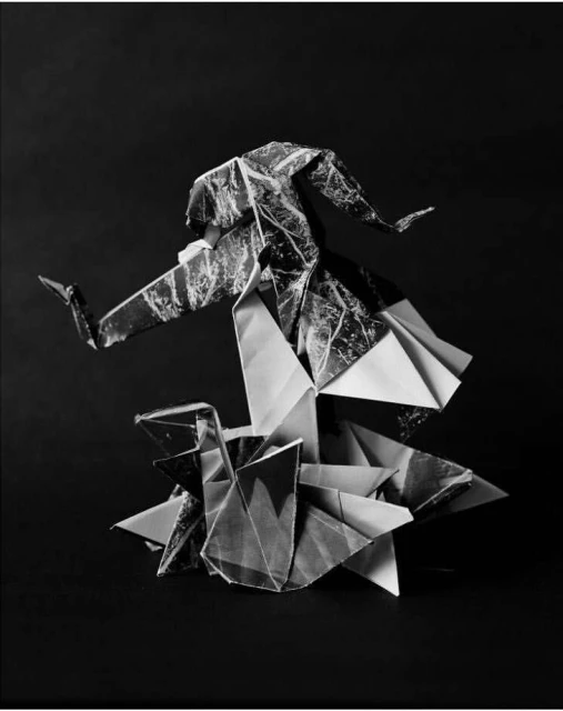 Origami sculpture of a dancing figure in black and white, constructed from folded paper, displayed against a dark background in studio lighting.