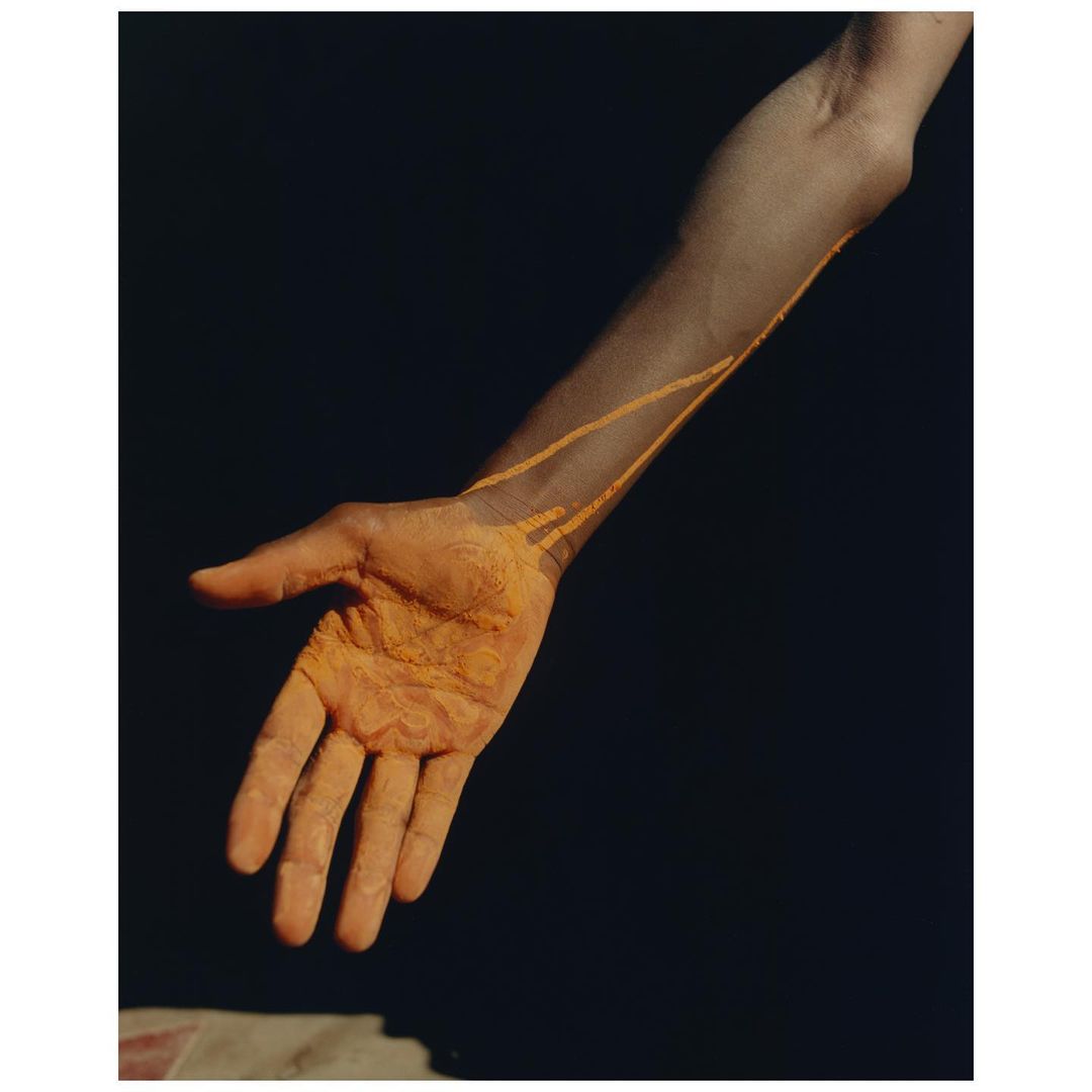Close-up studio shot featuring a person's forearm and hand, showcasing the model's tan skin against a dark background with painted lines.