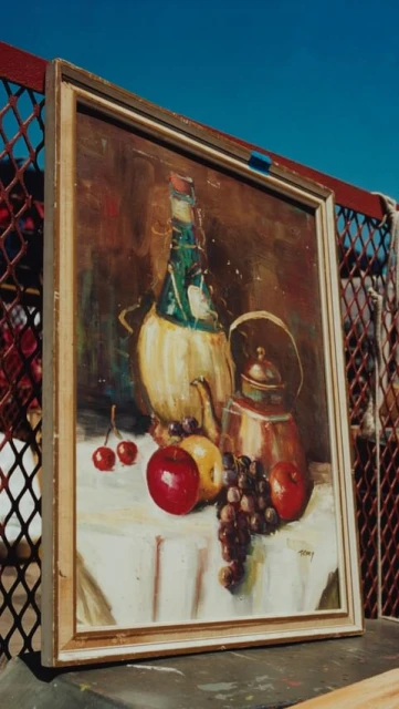Still life painting of a wine bottle, kettle, and fruits on a table with a white cloth, set against a bright blue sky.