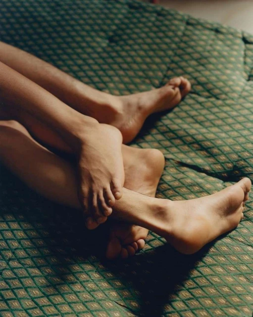 Close-up of the lower legs and feet of two people intertwined on a green patterned textile in an indoor setting with soft, diffused light.