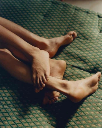 Close-up of the lower legs and feet of two people intertwined on a green patterned textile in an indoor setting with soft, diffused light.