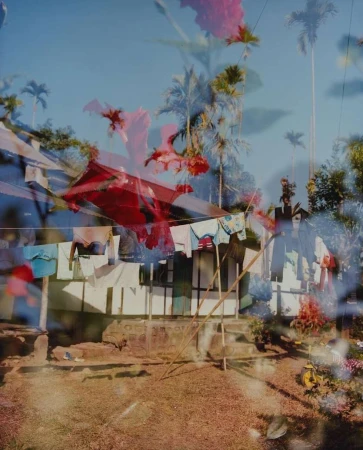Double exposure photograph featuring laundry hanging on a line outdoors with superimposed red flowers and palm trees in the background