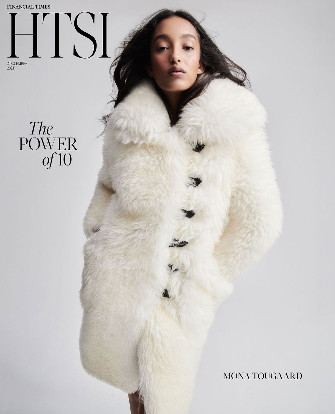 Magazine cover featuring a model wearing a large, white fur coat, with black buttons, posing in a studio with a neutral background.