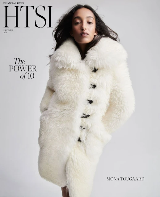Magazine cover featuring a model wearing a large, white fur coat, with black buttons, posing in a studio with a neutral background.