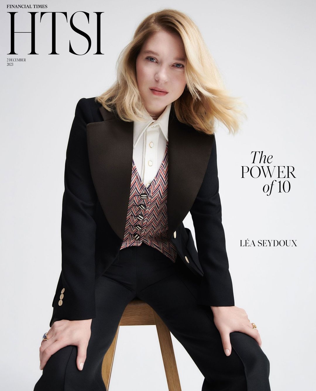 Magazine cover featuring Léa Seydoux in a black tuxedo and patterned vest, posing on a stool against a neutral backdrop.