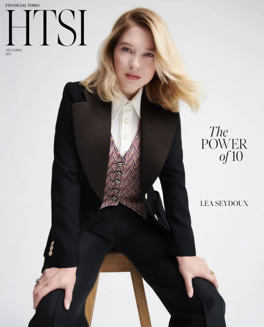 Magazine cover featuring Léa Seydoux in a black tuxedo and patterned vest, posing on a stool against a neutral backdrop.
