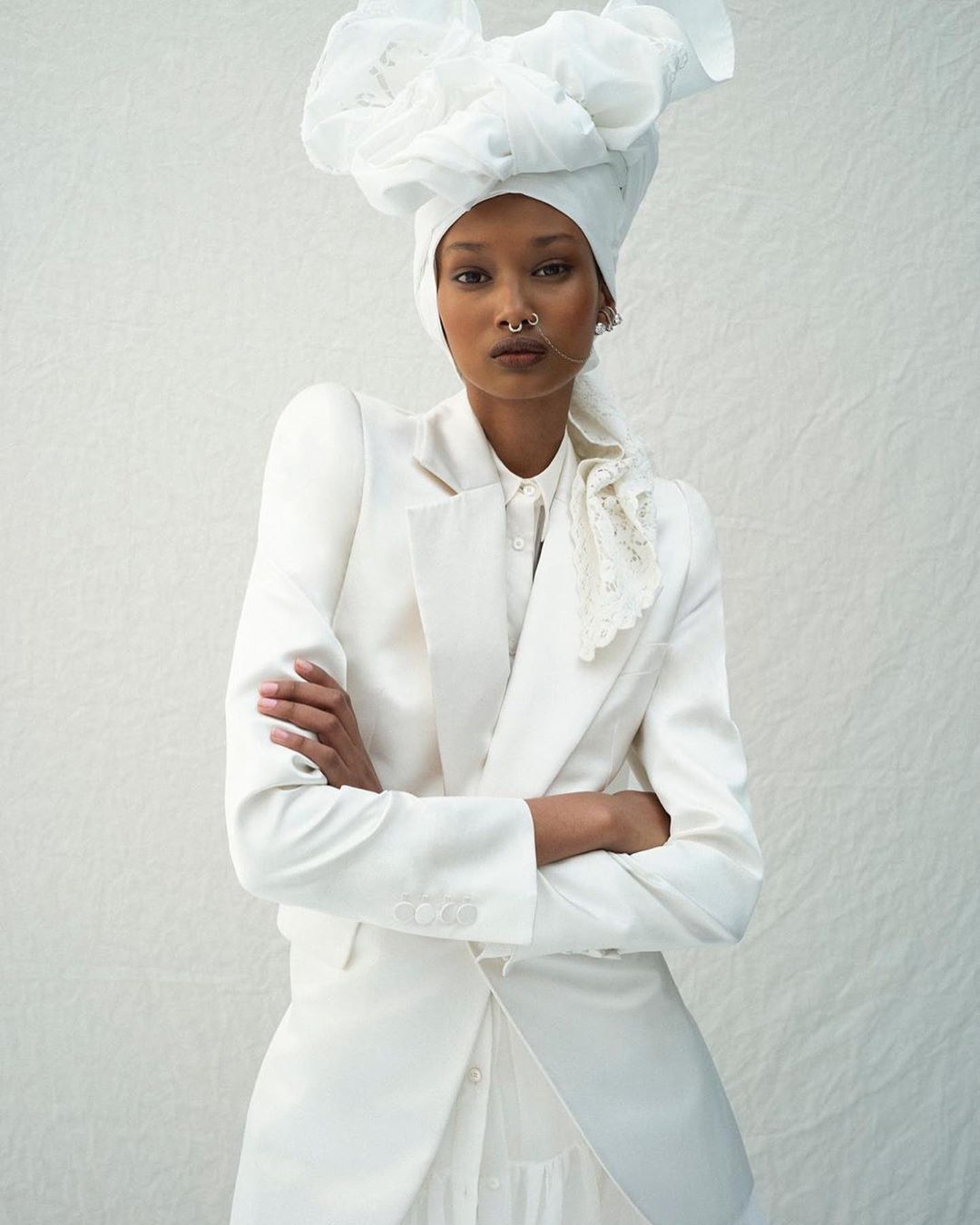 Woman in a white suit and white head covering poses in front of a white background. Beauty and fashion photography in a studio.