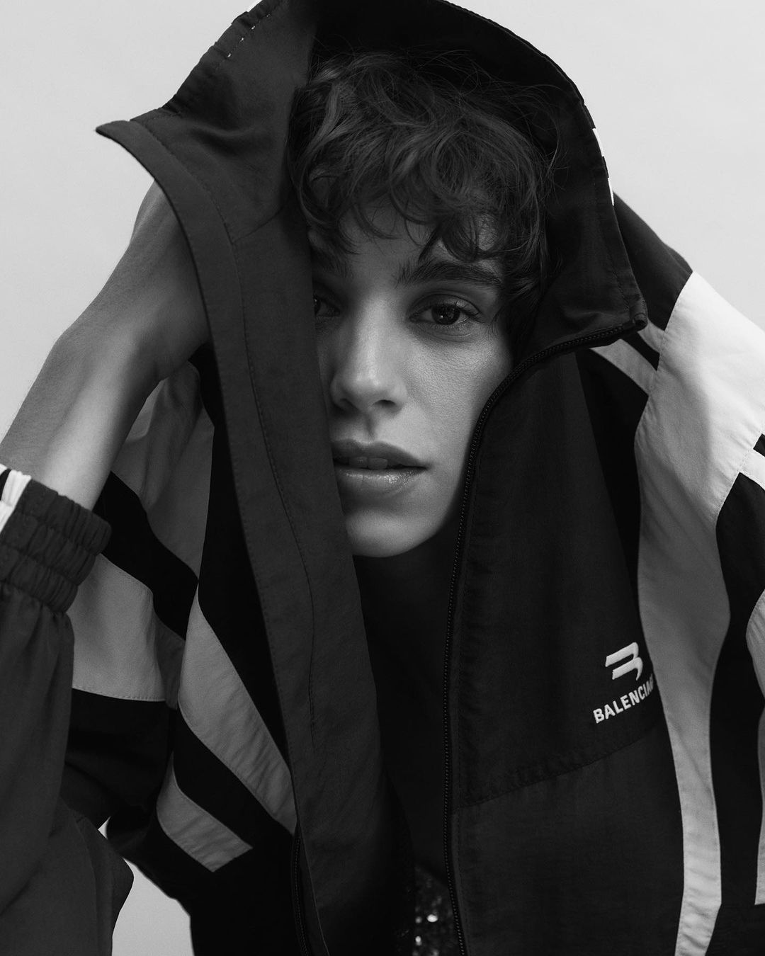 Monochrome portrait of a young adult wearing a black and white Balenciaga hooded jacket, face partially visible, neutral expression, studio lit.