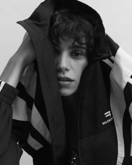Monochrome portrait of a young adult wearing a black and white Balenciaga hooded jacket, face partially visible, neutral expression, studio lit.