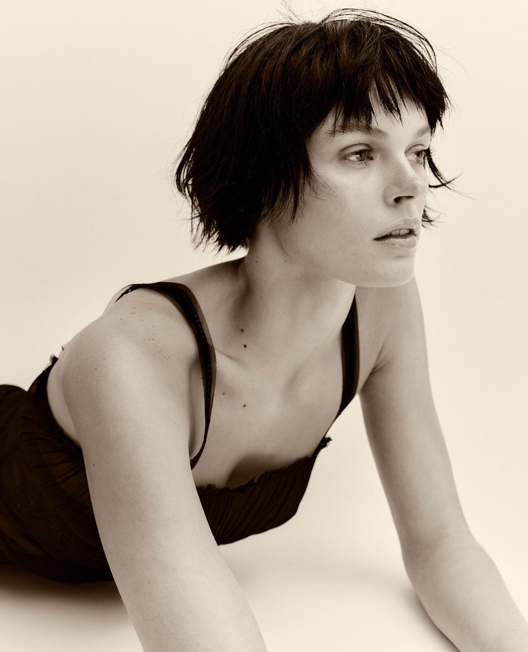 Close-up sepia portrait of a young adult woman with short dark hair, wearing a dark top, and posing in a photo studio setting.