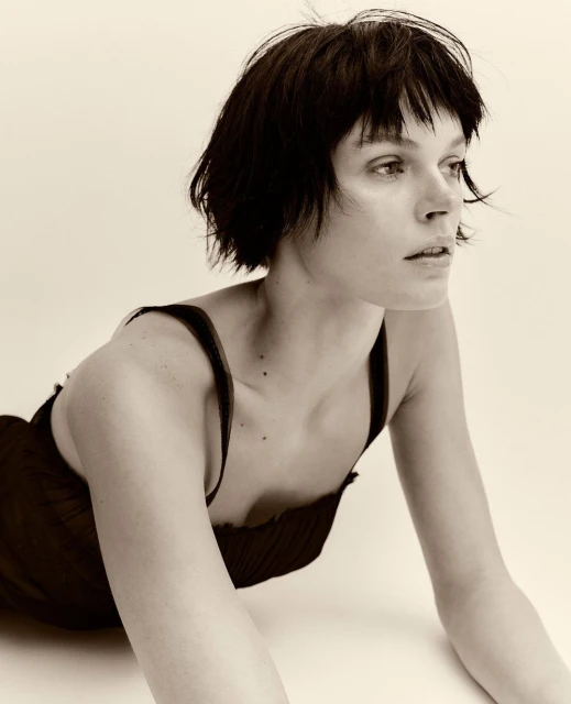 Close-up sepia portrait of a young adult woman with short dark hair, wearing a dark top, and posing in a photo studio setting.