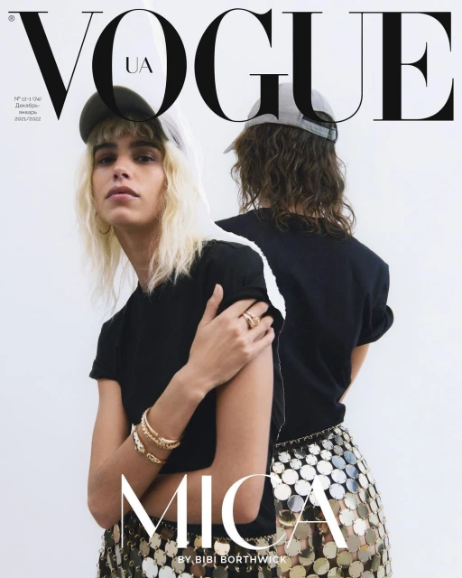 Two fashion models pose for a Vogue UA magazine cover, wearing black tops, metallic skirts, and baseball caps against a bright background.