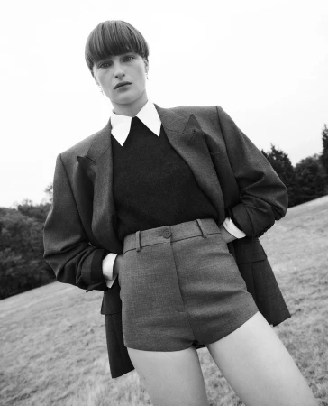 Model with bowl haircut wearing oversized blazer, white shirt, and shorts outdoors