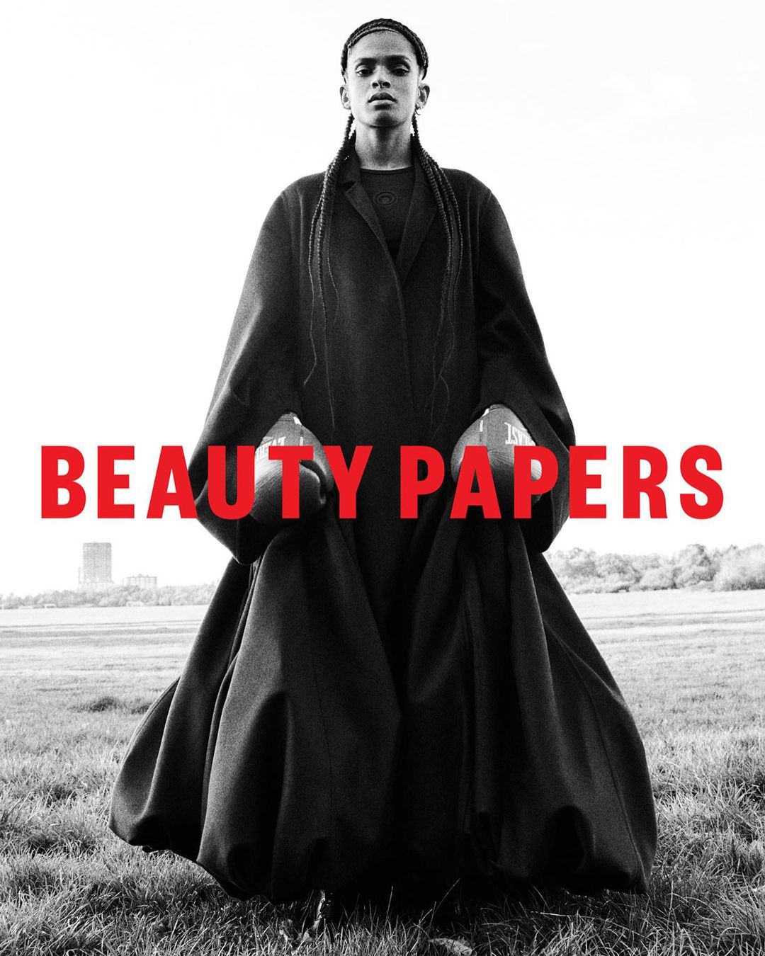Monochrome fashion portrait of a model wearing a heavy black coat and boxing gloves in a grassy field