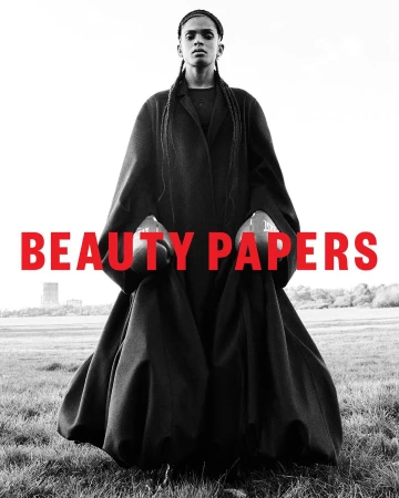 Monochrome fashion portrait of a model wearing a heavy black coat and boxing gloves in a grassy field