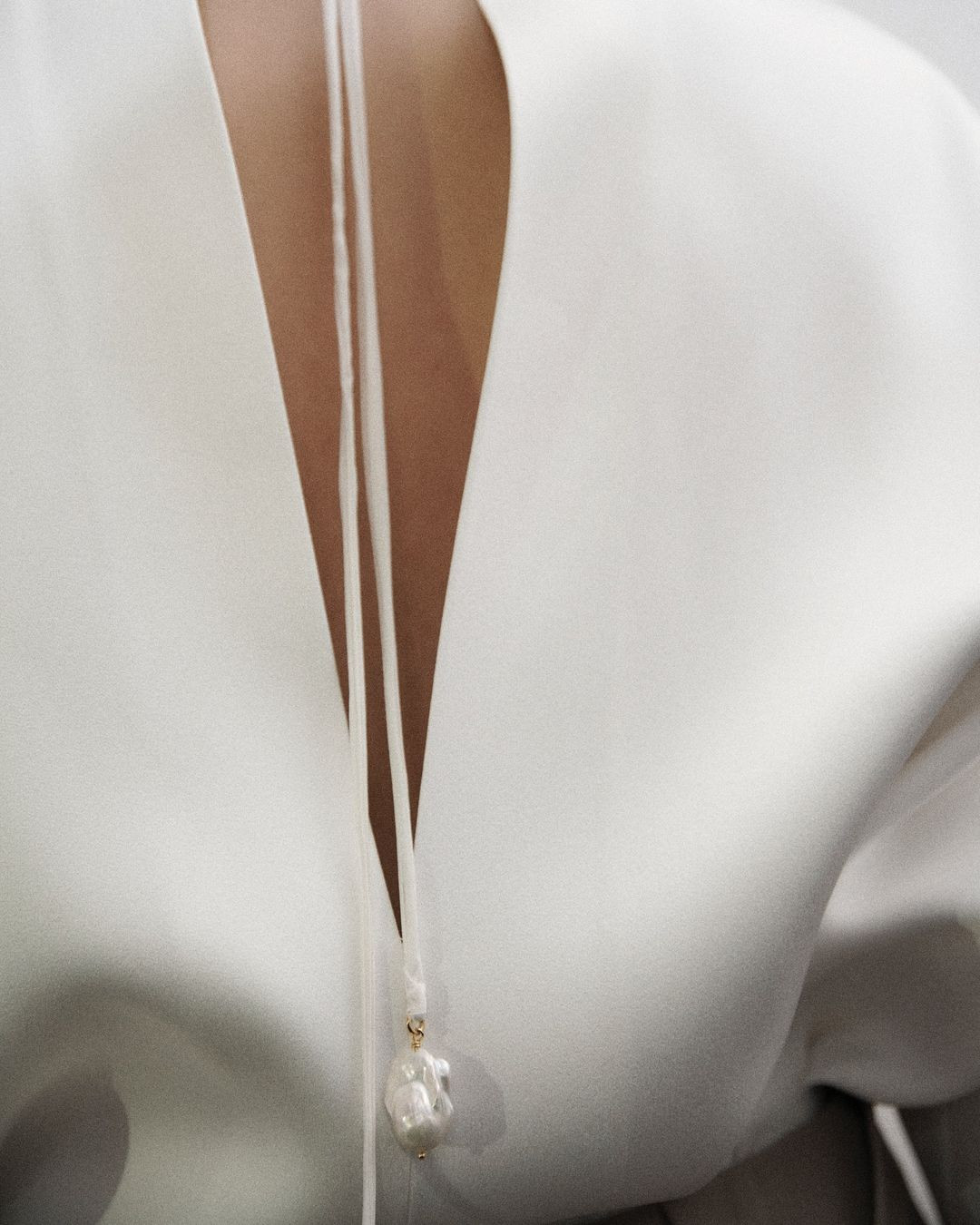 Close-up of a woman's back with white top and pearl pendant. The pendant hangs from thin white cords against the white top material.