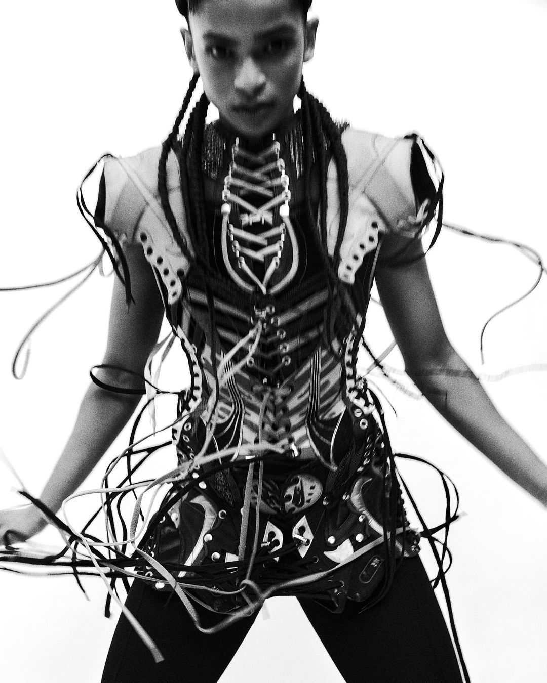 Monochrome portrait of a person in a heavily laced avant-garde corset top against a plain white background