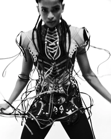 Monochrome portrait of a person in a heavily laced avant-garde corset top against a plain white background