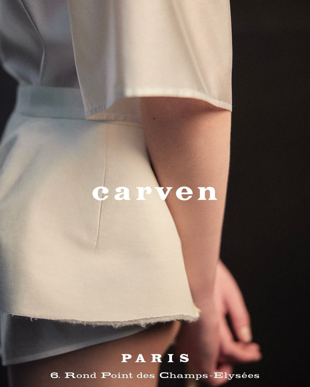 Fashion shot featuring a model wearing a white Carven skirt and top against a dark background, showcasing the brand's design.
