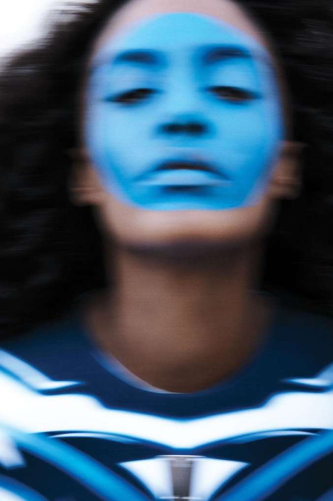 Abstract close-up portrait of a woman with blue face paint, set against a blurred background, with an artistic and surreal aesthetic.