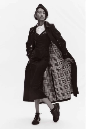 Black and white portrait of a model wearing a trench coat and beret against a plain white background by Bibi Cornejo Borthwick