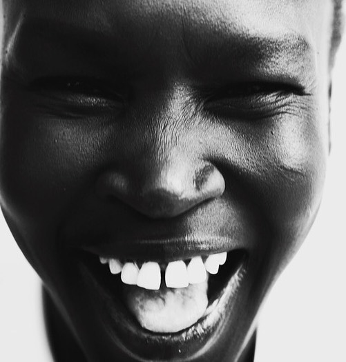 Black and white portrait of a smiling adult female with dark skin, bright white teeth, and closed eyes.