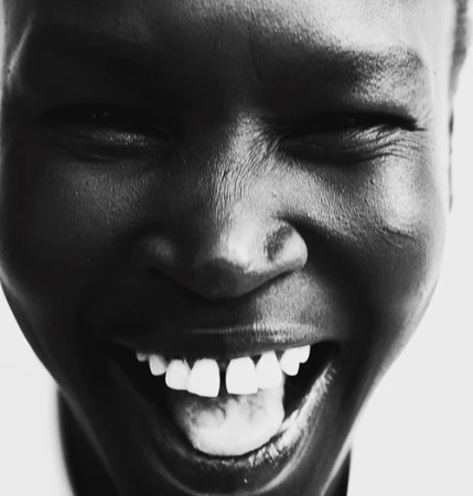 Close-up black and white portrait of a smiling Black woman showing teeth against a plain white background