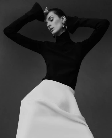 Model in black turtleneck and white skirt with hands raised to head photographed by Bibi Cornejo Borthwick