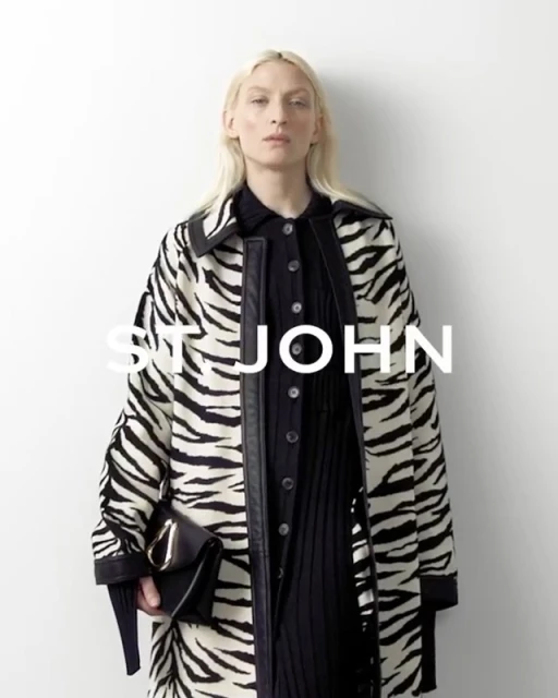 A blonde adult female model showcases a black and white zebra-striped coat, a black dress, and a black purse against a plain white background.