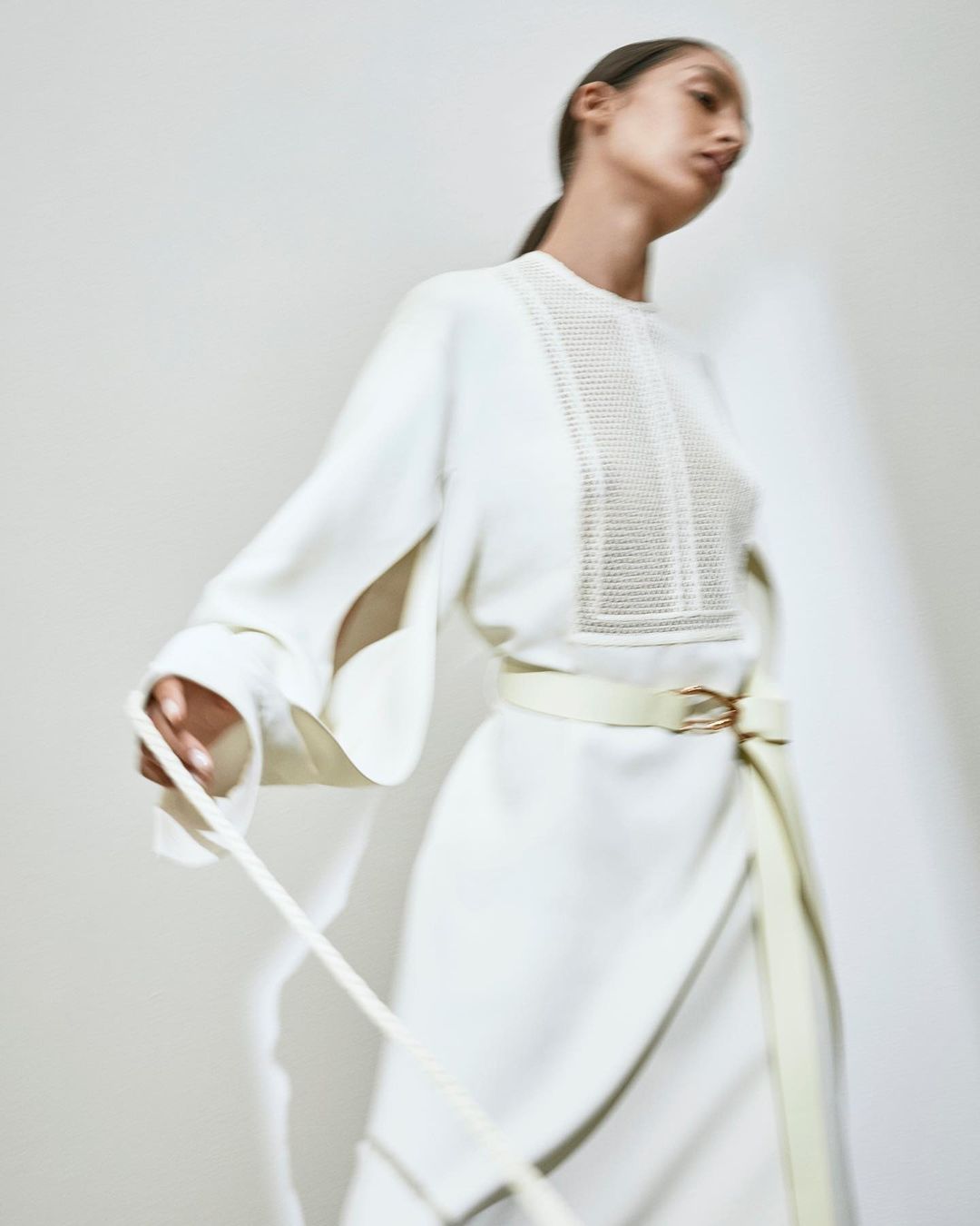 Model in a cream white long-sleeved dress with a belted waist against a neutral backdrop by Bibi Cornejo Borthwick