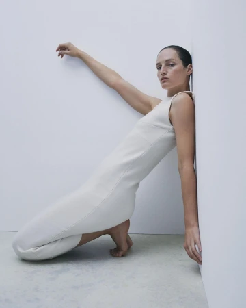 Model in sleeveless white dress leaning against a white studio wall, photographed by Bibi Cornejo Borthwick.