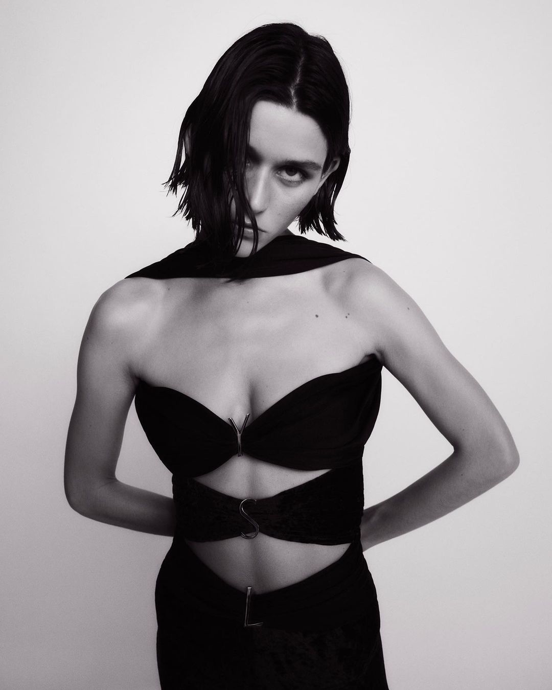Black and white portrait of a woman in a stylish black dress against a neutral background, highlighting her dark hair and striking features.
