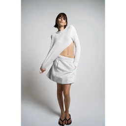 Model wearing a white ribbed knit sweater and white mini skirt standing against a plain light grey studio background.