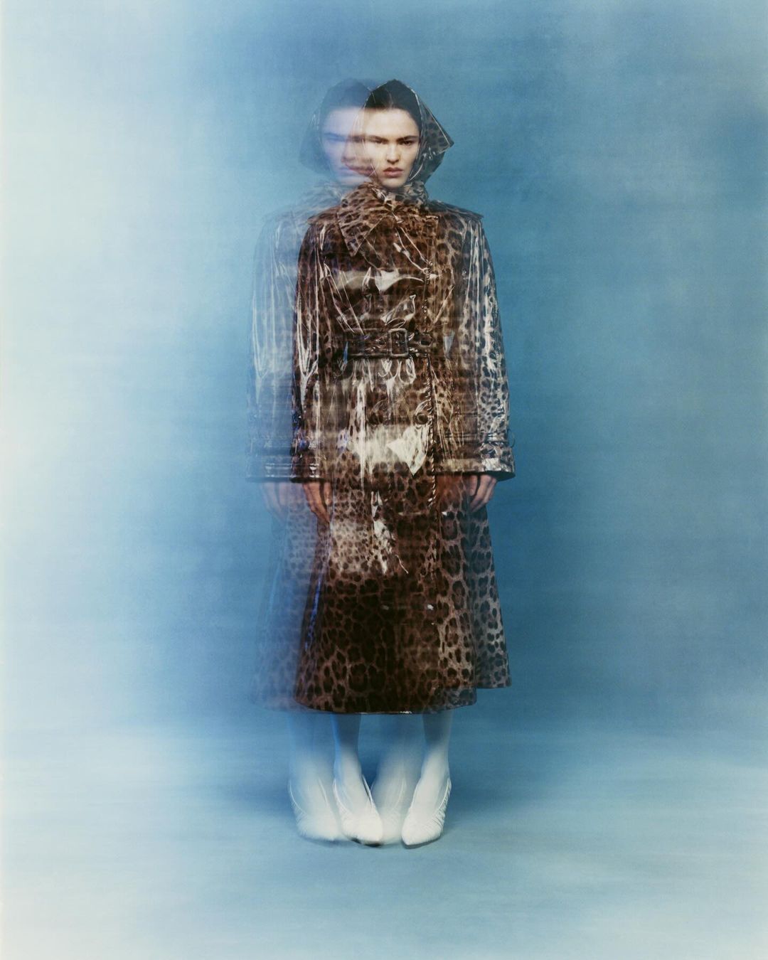 Fashion portrait of a woman wearing a leopard-print coat and white shoes against a blurred blue background with motion blur effects.